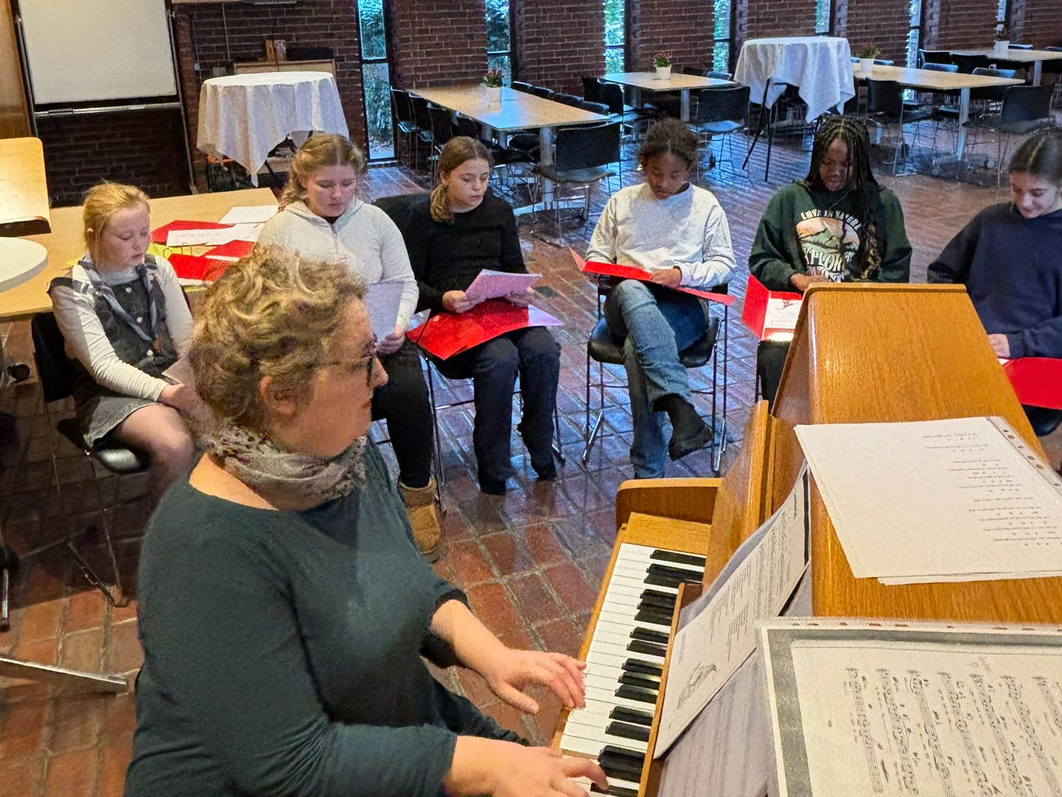 Børnene sidder rundt om klaveret og synger. Dirigenten spiller.