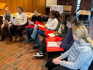 Børnene sidder rundt om klaveret og synger. Dirigenten spiller.